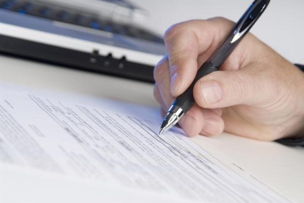 man holding a pen writing a signature, computer in background